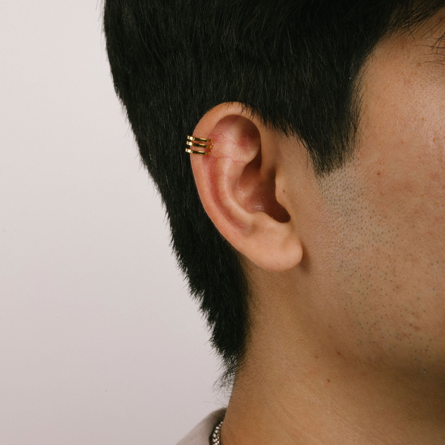A model wearing the Triple Band Ear Cuff features a secure medium hold, adjustable fit, and non-tarnish, water-resistant stainless steel and titanium construction. Its 9mm diameter and 6mm width makes it ideal for all ear types, including thick/large, sensitive, small/thin, and stretched/healing ears. Average comfortable wear duration is up to 24 hours for one piece. Intended to be worn on the helix of the ear.