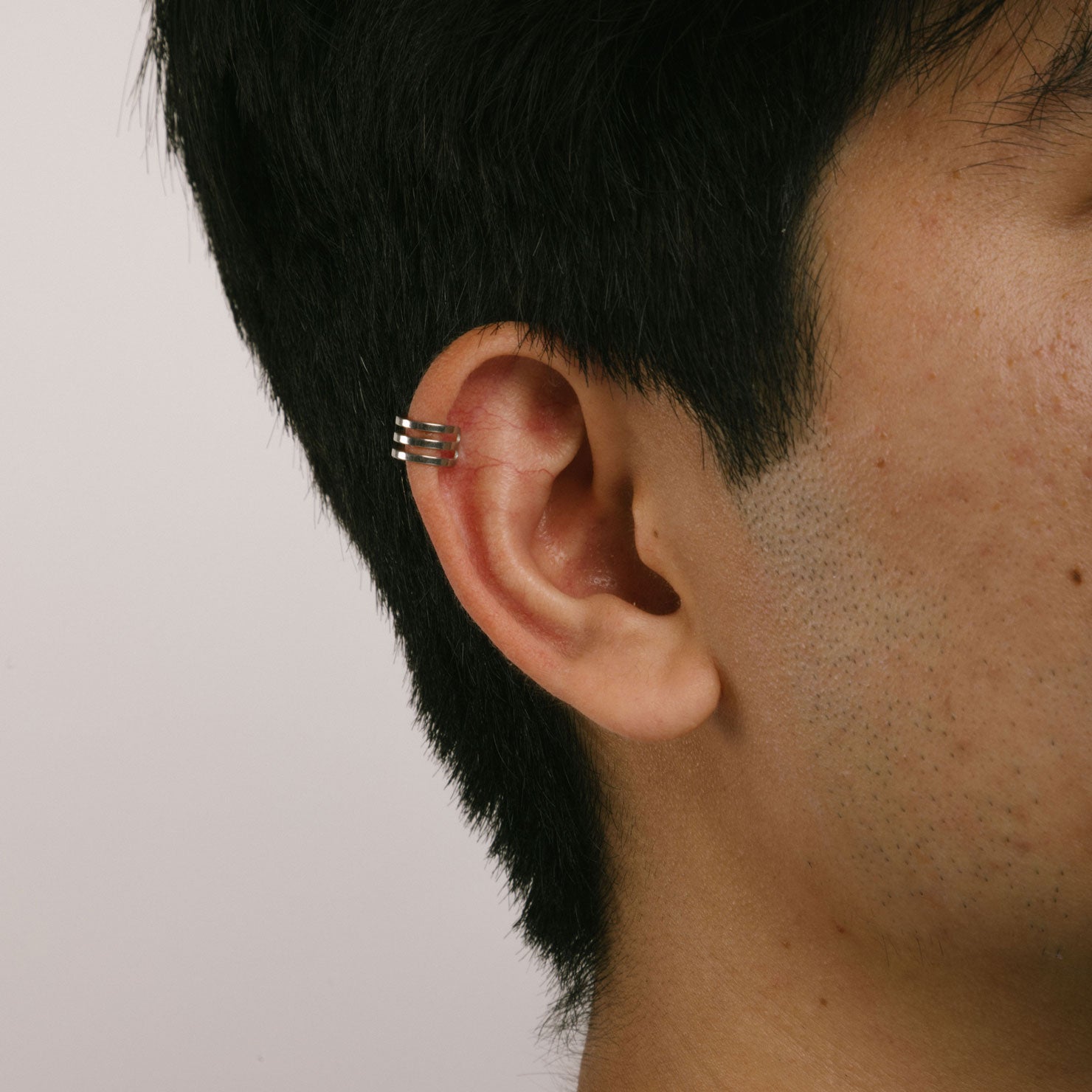 A model wearing the Triple Band Ear Cuff features a secure medium hold, adjustable fit, and non-tarnish, water-resistant stainless steel and titanium construction. Its 9mm diameter and 6mm width makes it ideal for all ear types, including thick/large, sensitive, small/thin, and stretched/healing ears. Average comfortable wear duration is up to 24 hours for one piece. Intended to be worn on the helix of the ear.