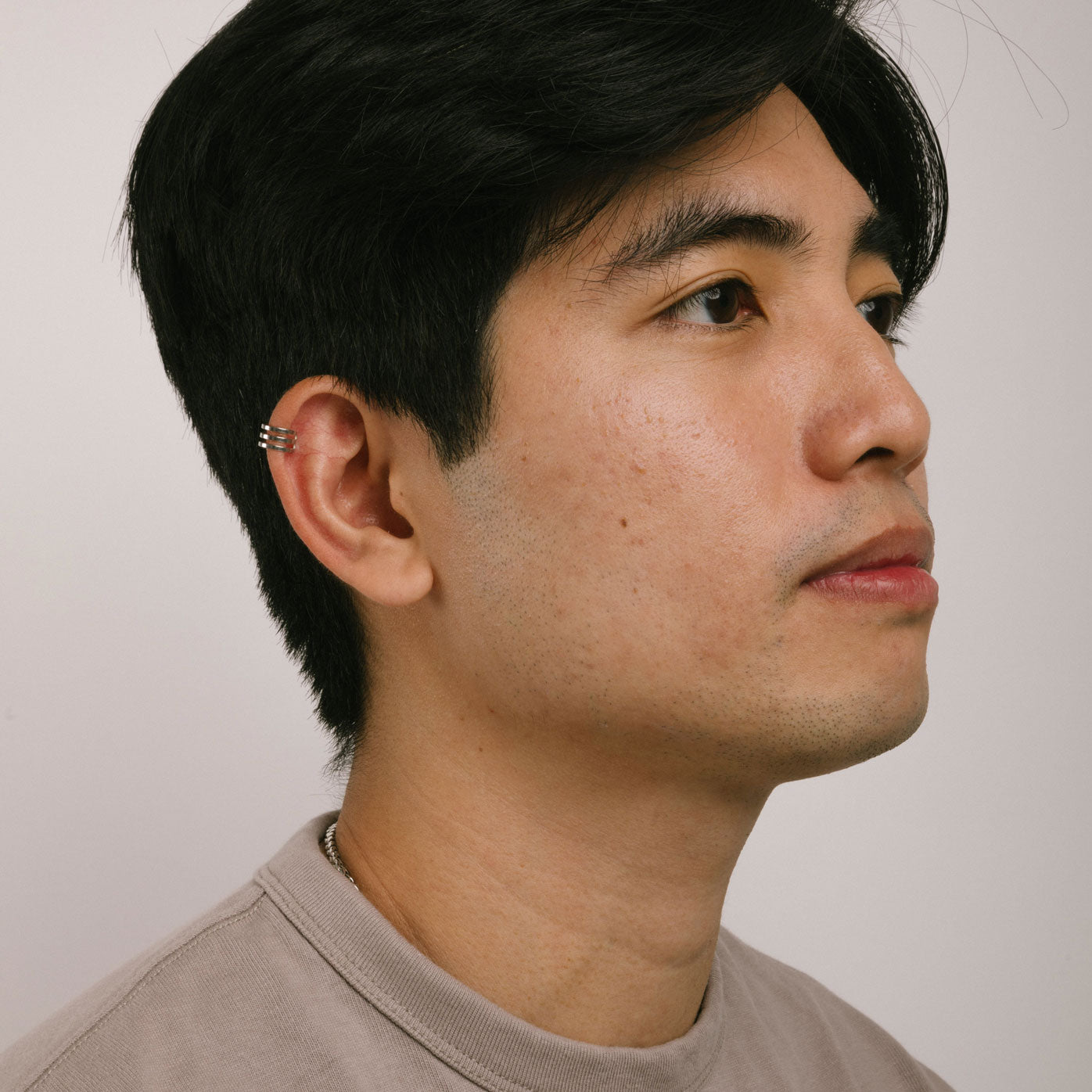 A model wearing the Triple Band Ear Cuff features a secure medium hold, adjustable fit, and non-tarnish, water-resistant stainless steel and titanium construction. Its 9mm diameter and 6mm width makes it ideal for all ear types, including thick/large, sensitive, small/thin, and stretched/healing ears. Average comfortable wear duration is up to 24 hours for one piece. Intended to be worn on the helix of the ear.