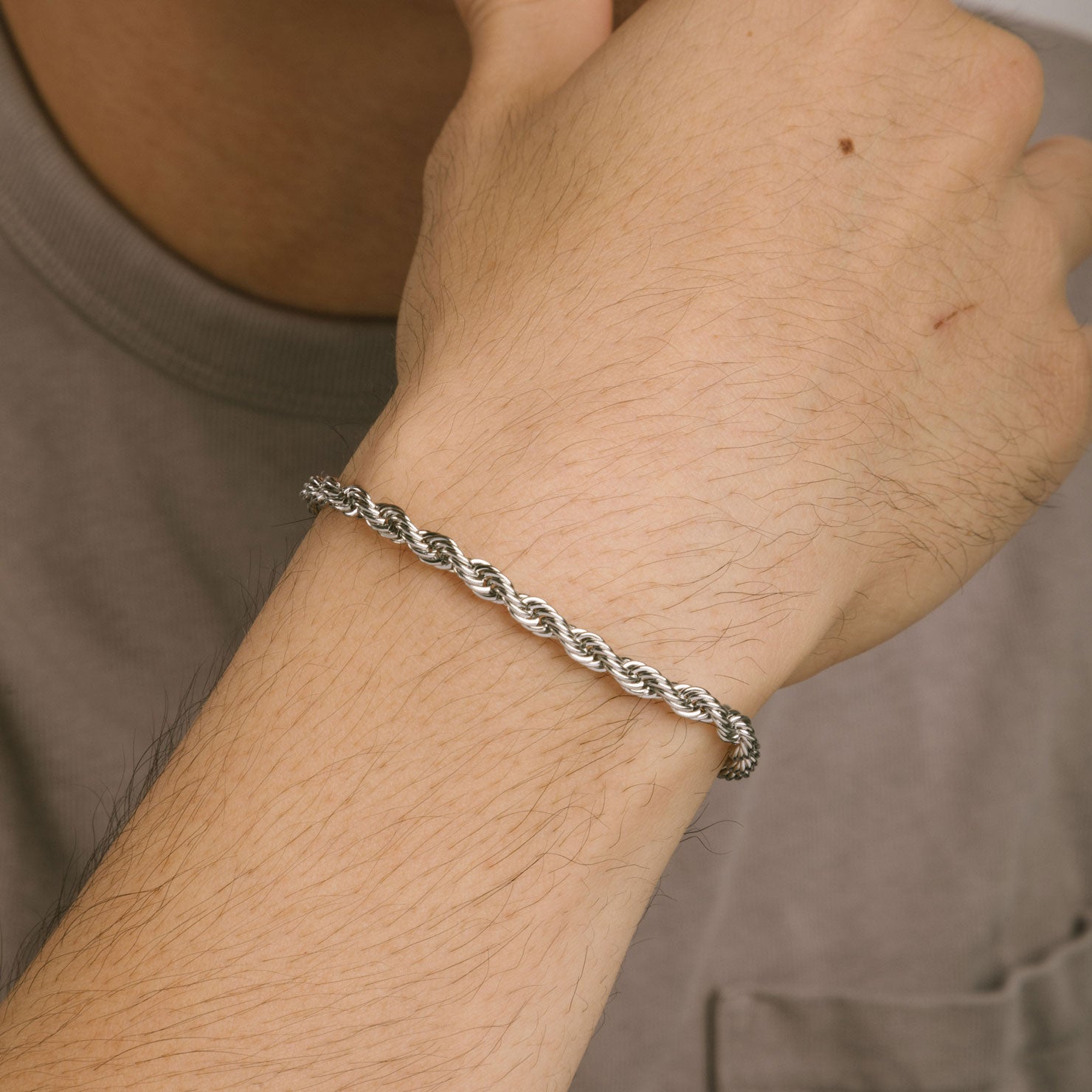 A model wearing the Twist Rope Chain Bracelet in Silver is crafted from non-tarnish and water-resistant stainless steel, with dimensions of 18 cm in length and 4 mm in width.