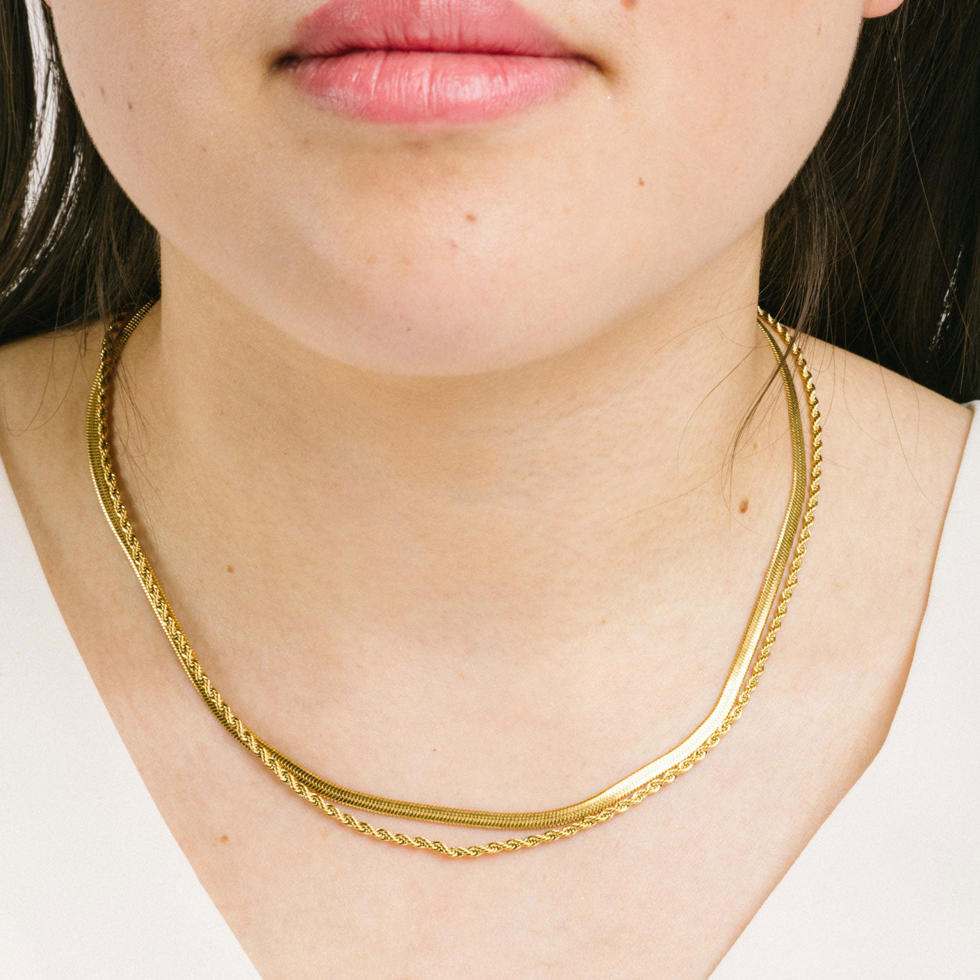 A model wearing the Twisted Double Layered Necklace consists of 14K Gold Plated Stainless Steel, providing water resistance, non-tarnishing, and leading, nickel, and cadmium free properties. Additionally, it is adjustable, though only one necklace is included.