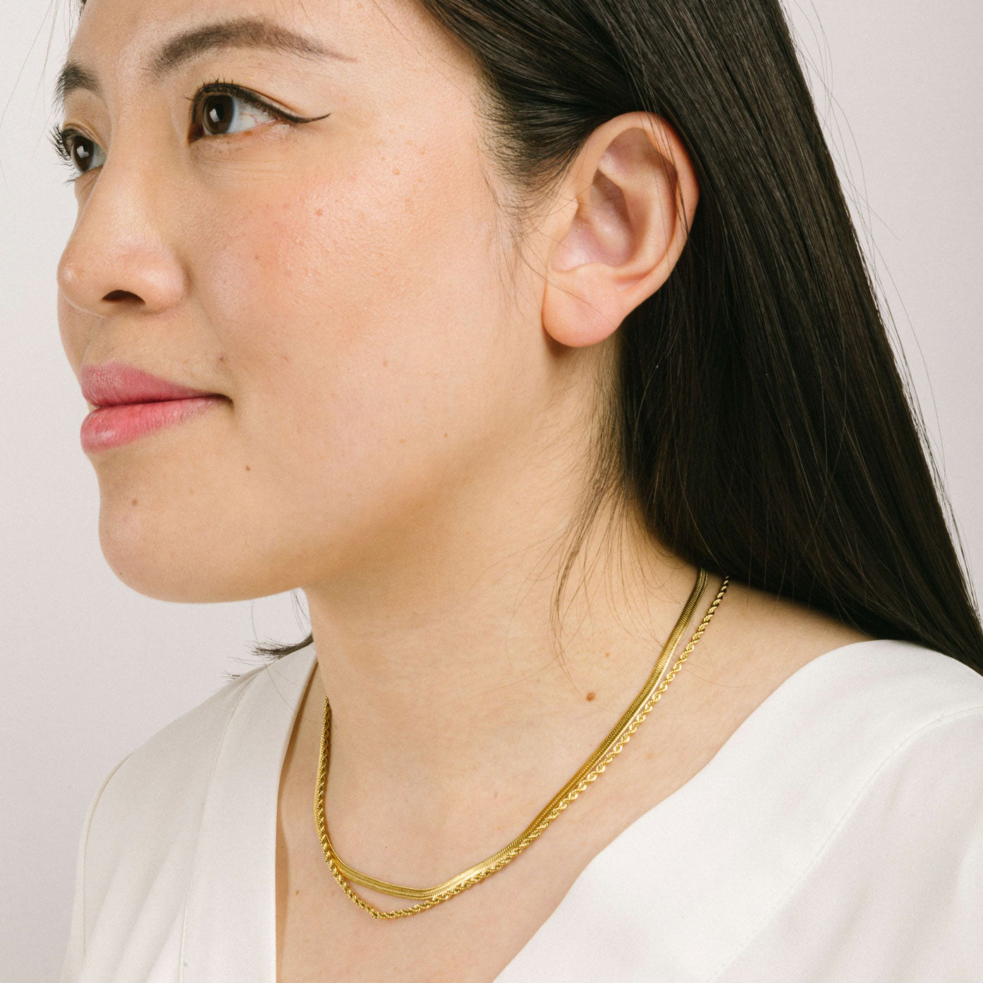 A model wearing the Twisted Double Layered Necklace consists of 14K Gold Plated Stainless Steel, providing water resistance, non-tarnishing, and leading, nickel, and cadmium free properties. Additionally, it is adjustable, though only one necklace is included.