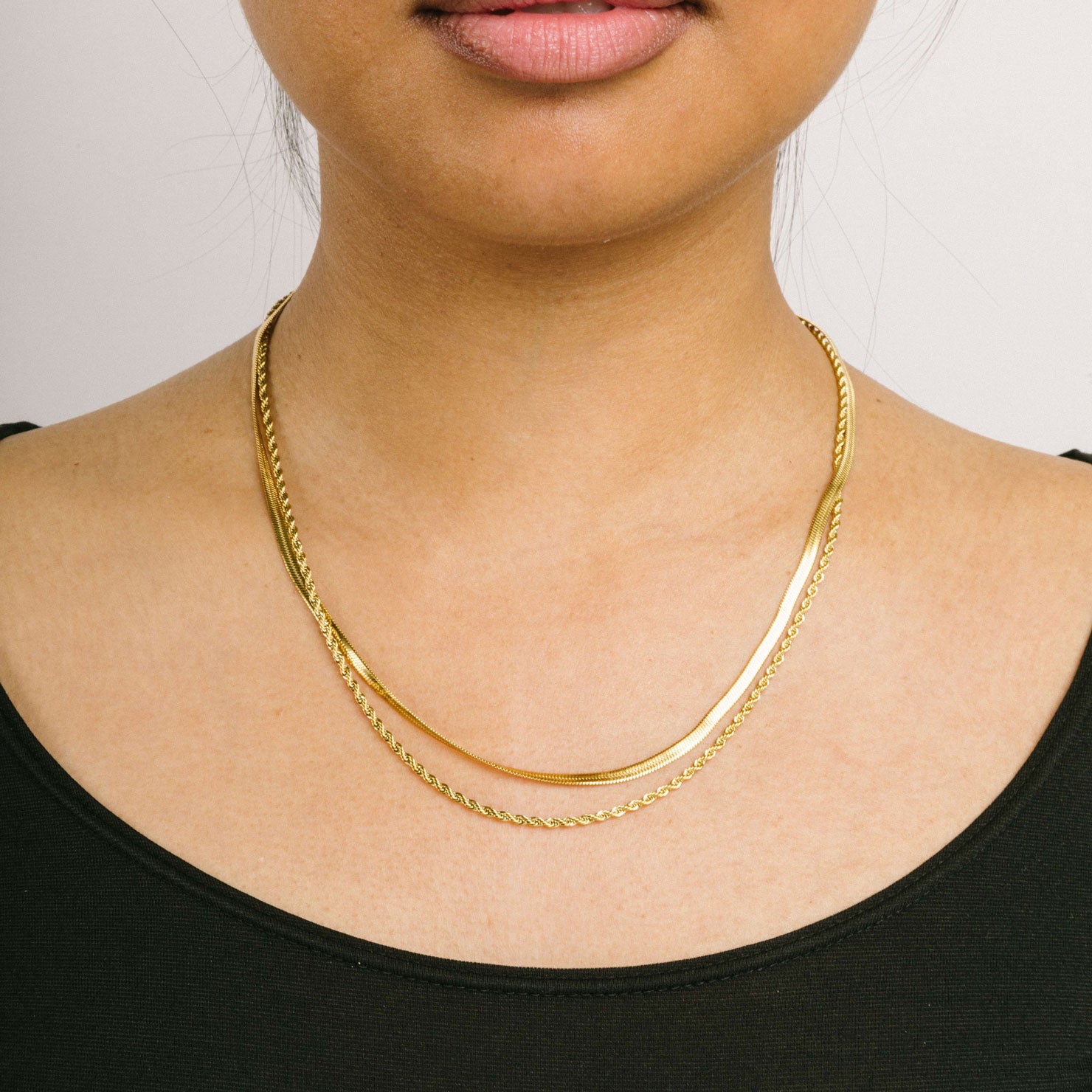 A model wearing the Twisted Double Layered Necklace consists of 14K Gold Plated Stainless Steel, providing water resistance, non-tarnishing, and leading, nickel, and cadmium free properties. Additionally, it is adjustable, though only one necklace is included.