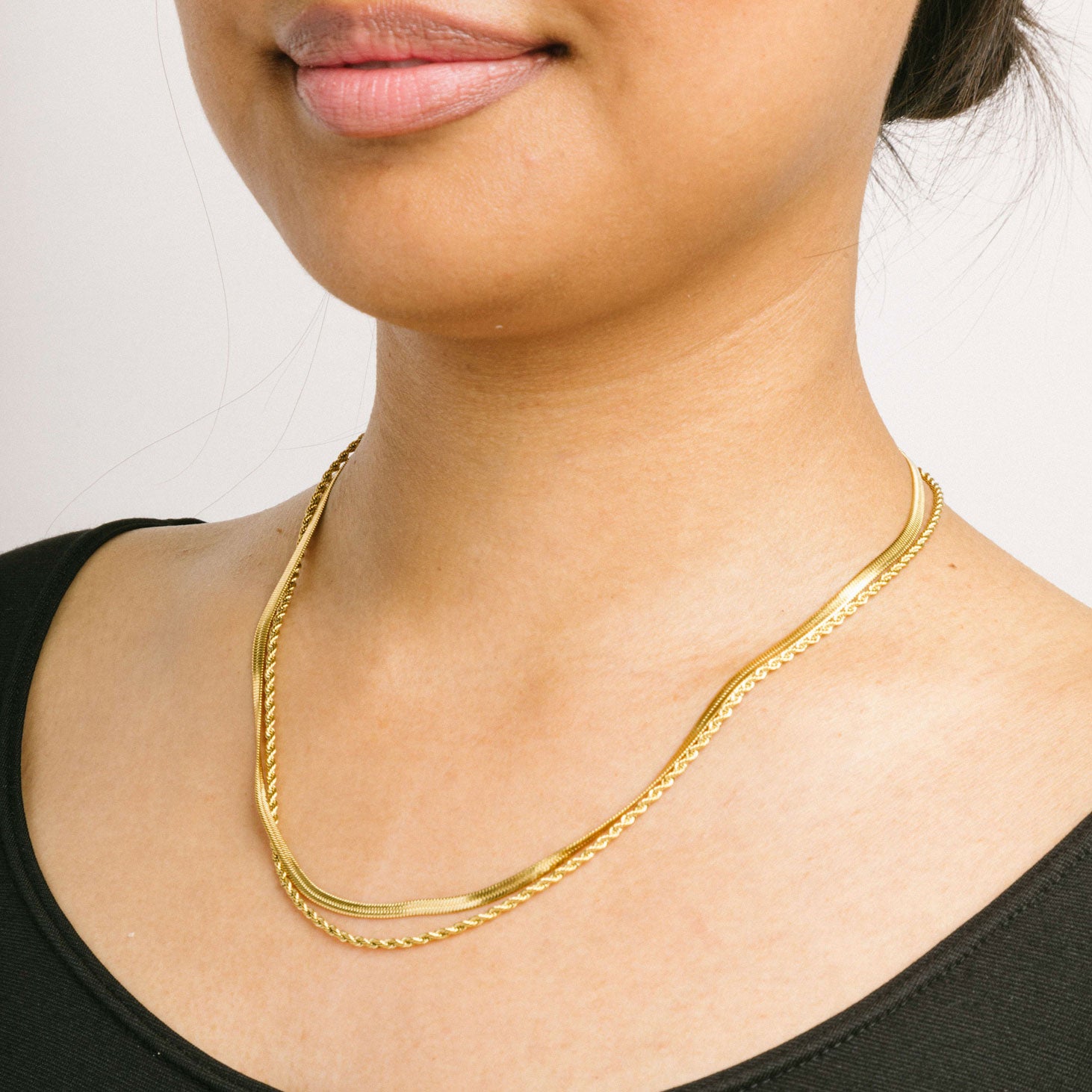 A model wearing the Twisted Double Layered Necklace consists of 14K Gold Plated Stainless Steel, providing water resistance, non-tarnishing, and leading, nickel, and cadmium free properties. Additionally, it is adjustable, though only one necklace is included.