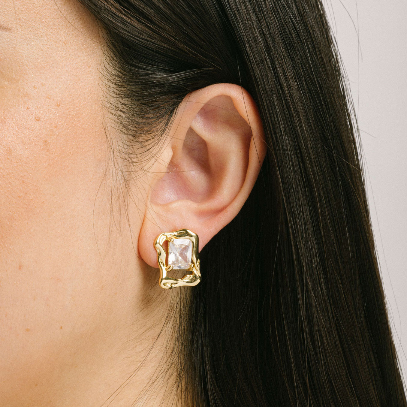 A model wearing the Valerie Clip On Earrings in Gold feature a padded clip-on closure for secure hold and comfortable wear up to 12 hours. These earrings are crafted with gold tone copper alloy and cubic zirconia, and can be worn by all ear types, including thick/large ears, sensitive ears, small/thin ears, and stretched/healing ears. Please note: one pair is included.