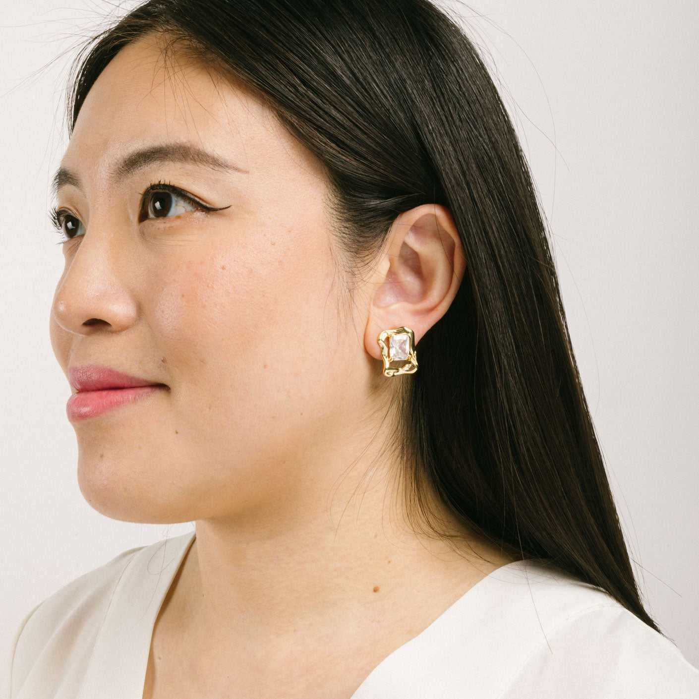 A model wearing the Valerie Clip On Earrings in Gold feature a padded clip-on closure for secure hold and comfortable wear up to 12 hours. These earrings are crafted with gold tone copper alloy and cubic zirconia, and can be worn by all ear types, including thick/large ears, sensitive ears, small/thin ears, and stretched/healing ears. Please note: one pair is included.
