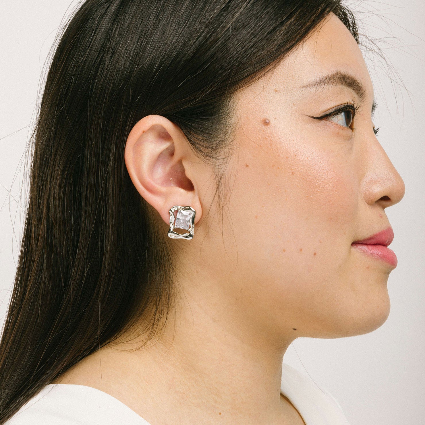 A model wearing the Valerie Clip On Earrings in Silver offer a secure hold for up to 12 hours of comfortable wear. Featuring a padded clip-on design, these earrings are ideal for all ear types, including those that are thick and large, sensitive, small and thin, or stretched and healing. Crafted with a silver tone copper alloy and cubic zirconia, each order includes one pair.