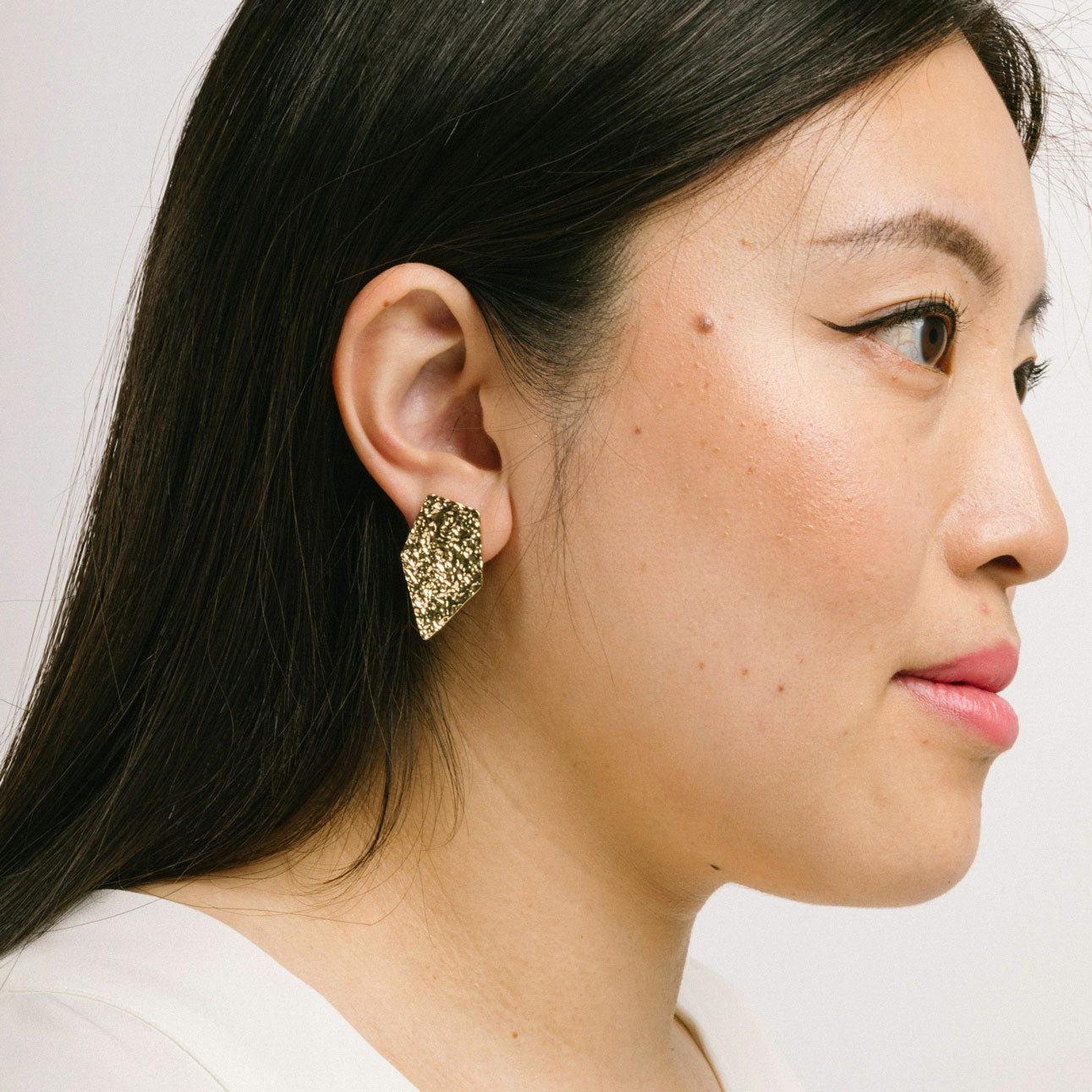 A model wearing the Vesper Clip On Earrings in Gold boast a secure padded clip-on closure, suitable for all ear types, with hold strength designed to last 8-12 hours. Crafted from zinc alloy and copper alloy, this single pair is adjustable and comfortable to wear.