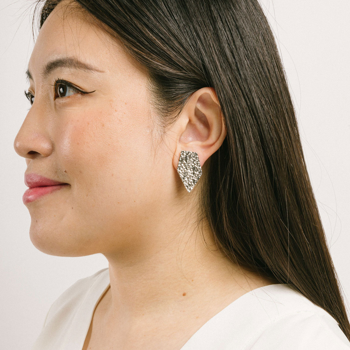 A model wearing the Vesper Clip On Earrings in Silver are padded clip-on earrings with a secure hold. Perfect for all ear types, they offer a comfortable wear for 8-12 hours. Made of zinc and copper alloy, the earrings come with a removable black rubber padding and can be worn as pictured. Please note, item is sold as one pair.