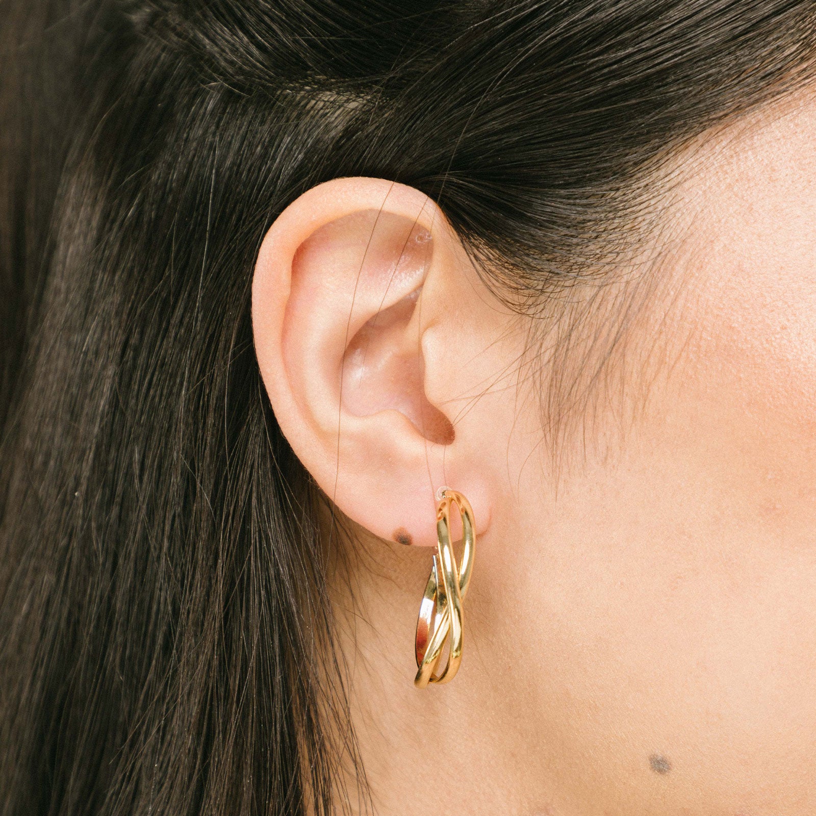 A model wearing the Gold Vienna Hoop Clip-On Earrings feature a resin clip-on closure with medium secure hold. The earrings are suitable for all types of ears, with an average comfortable wear time of 8-12 hours. No adjustments can be made. Constructed with gold tone metal alloy, these earrings are also available in silver.