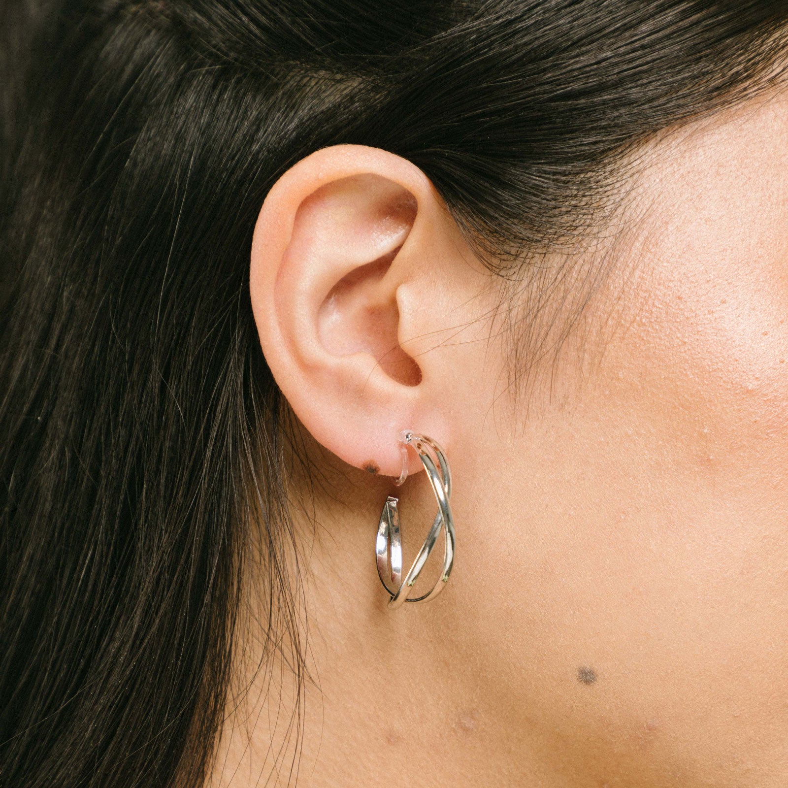 A model wearing the Silver Vienna Hoop Clip-On Earrings are crafted of Silver Tone Metal Alloy and feature a resin clip-on closure. These earrings are suited for all ear types, providing a medium-secure hold and an 8-12 hour average comfortable wear duration. Adjustment is not possible for this item; it is sold as a single pair in gold and silver.
