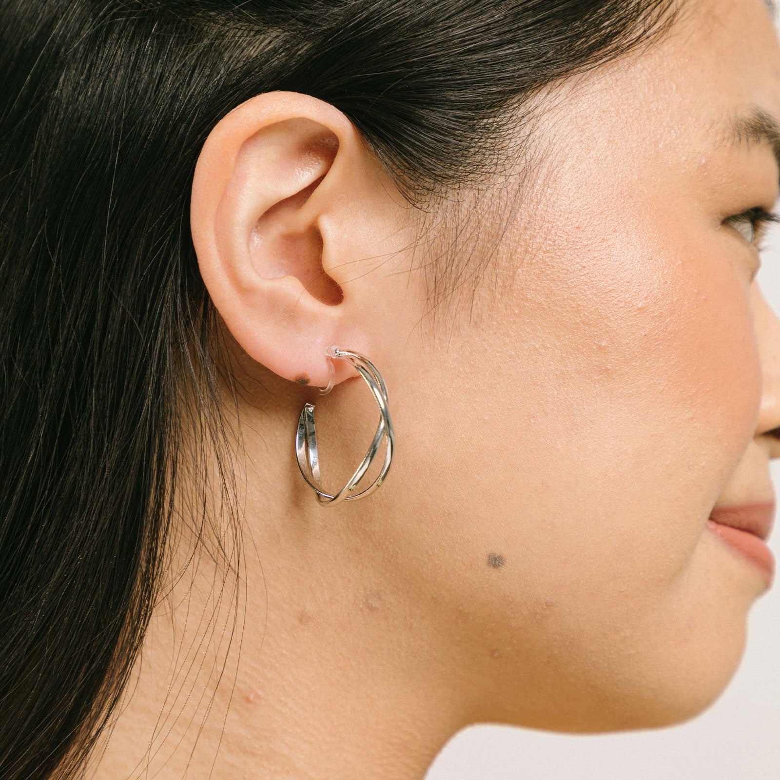A model wearing the Silver Vienna Hoop Clip-On Earrings are crafted of Silver Tone Metal Alloy and feature a resin clip-on closure. These earrings are suited for all ear types, providing a medium-secure hold and an 8-12 hour average comfortable wear duration. Adjustment is not possible for this item; it is sold as a single pair in gold and silver.