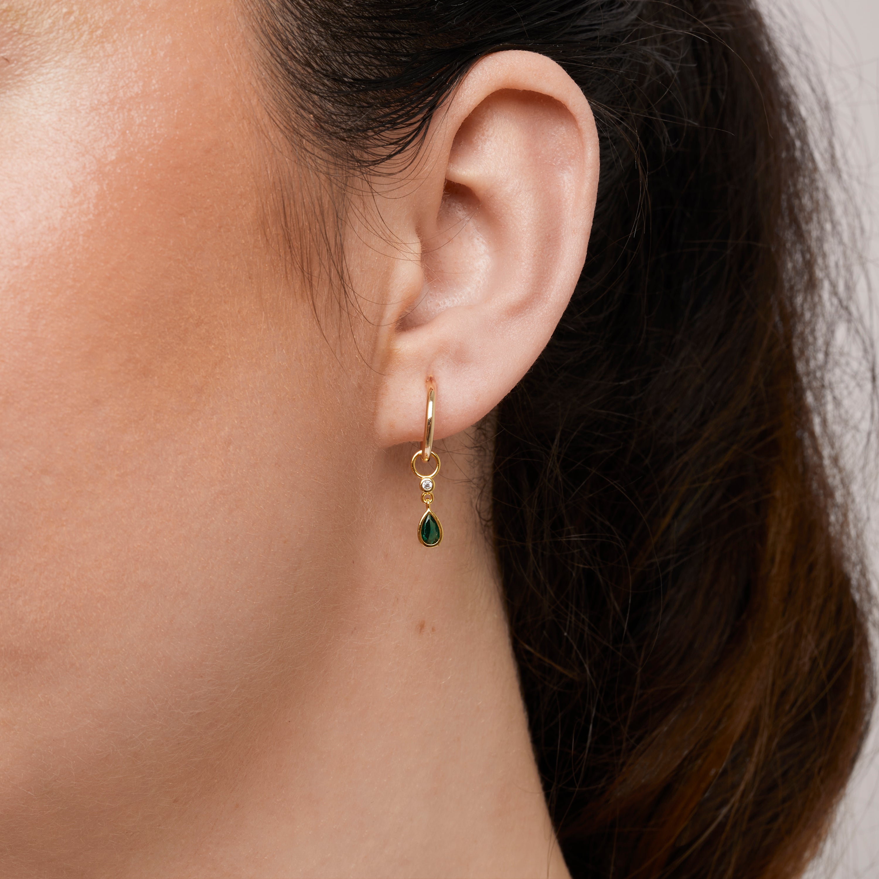 A model wearing the Emerald Drop Hoop Charms are made with high-quality materials, including 18K gold plating over 925 Sterling Silver. These charms are both non-tarnish and water resistant. The perfect combination of style and durability.