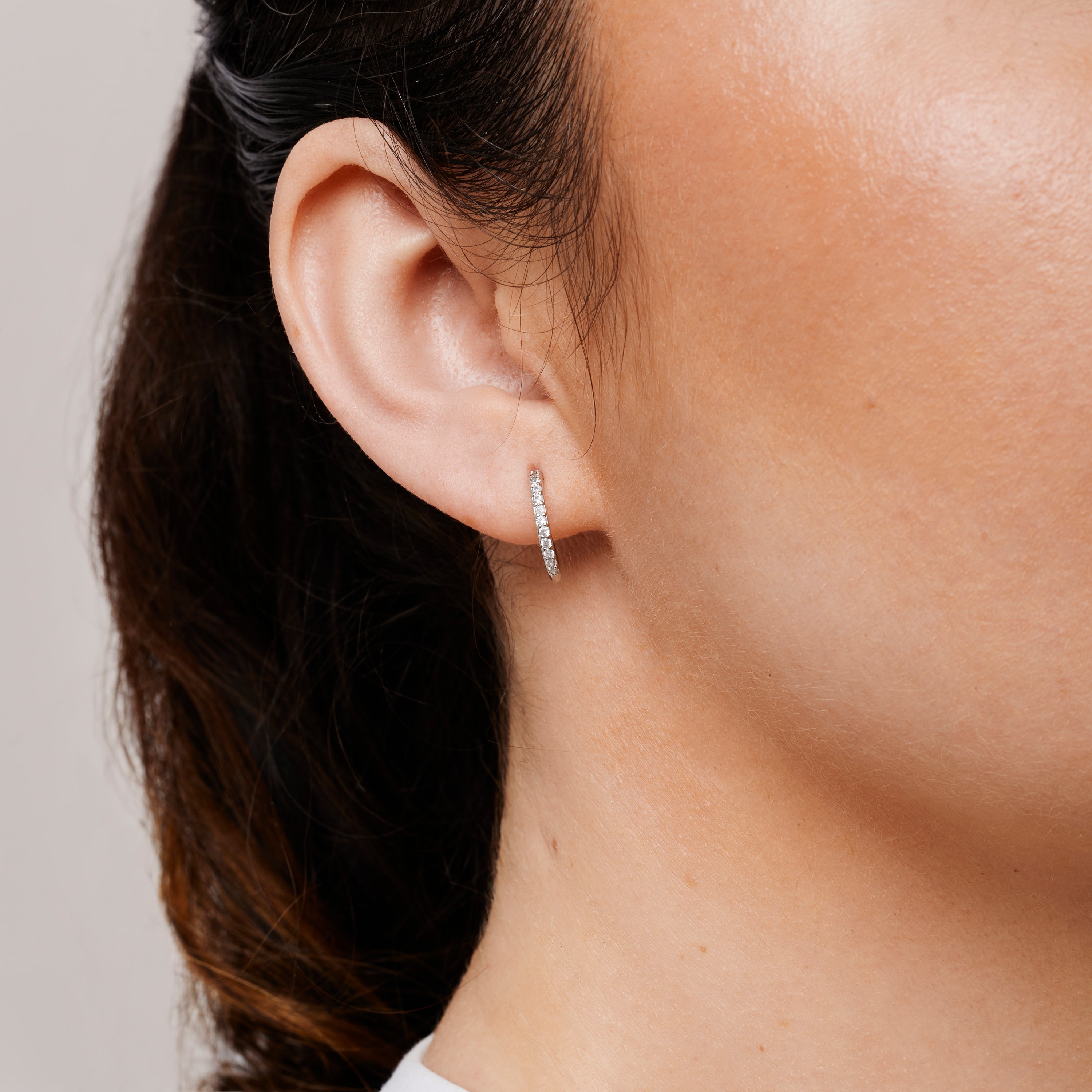 A model wearing the Medium Pavé Hoop Clip On Earrings in Silver offer a Mosquito Coil Clip-On Closure, making them ideal for Thick/Large Ears, Sensitive Ears, Small/Thin Ears, Stretched/Healing Ears, and Keloid Prone Ears. They provide an average comfortable wear duration of 24 hours with a medium secure hold, and can be gently adjusted by squeezing the padding forward once on the ear. Please note that this item is only one pair.