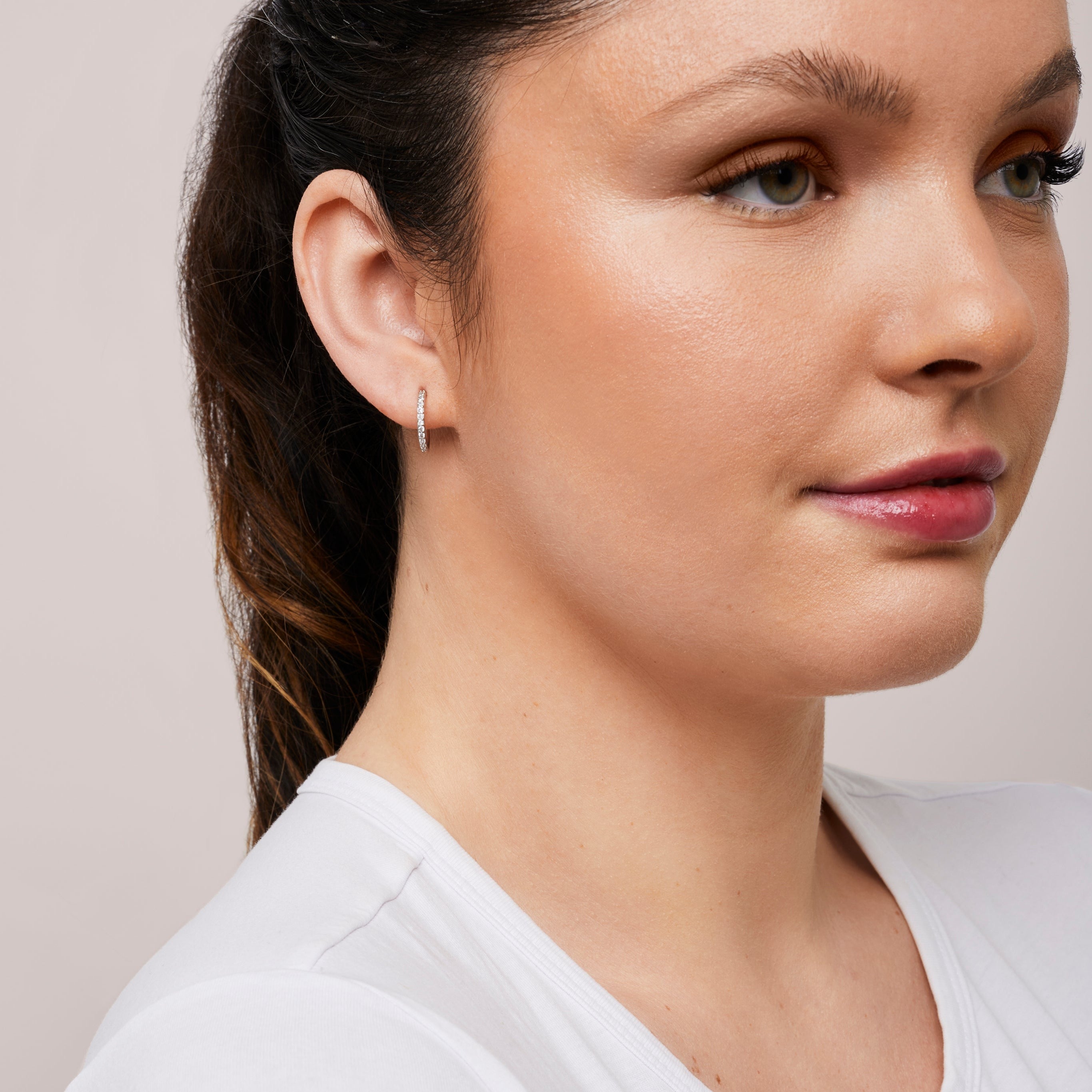 A model wearing the Medium Pavé Hoop Clip On Earrings in Silver offer a Mosquito Coil Clip-On Closure, making them ideal for Thick/Large Ears, Sensitive Ears, Small/Thin Ears, Stretched/Healing Ears, and Keloid Prone Ears. They provide an average comfortable wear duration of 24 hours with a medium secure hold, and can be gently adjusted by squeezing the padding forward once on the ear. Please note that this item is only one pair.