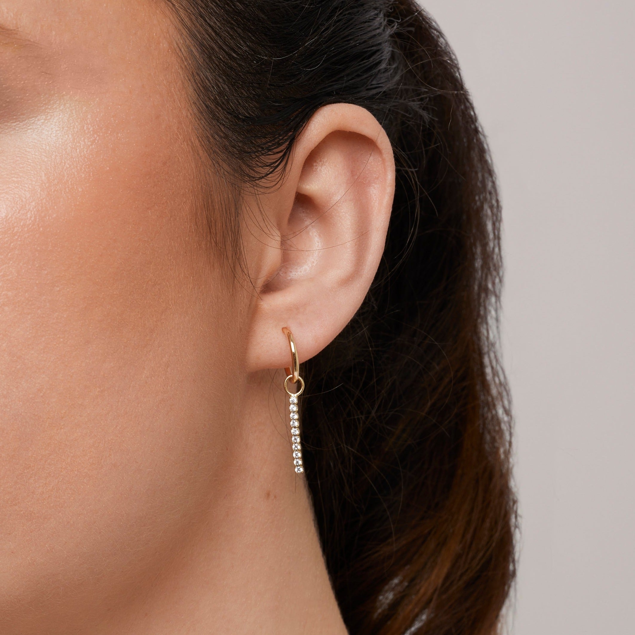 A model wearing the Pavé Bar Hoop Charms are made with high-quality materials, including 18K gold plating over 925 Sterling Silver. These charms are both non-tarnish and water resistant. The perfect combination of style and durability.