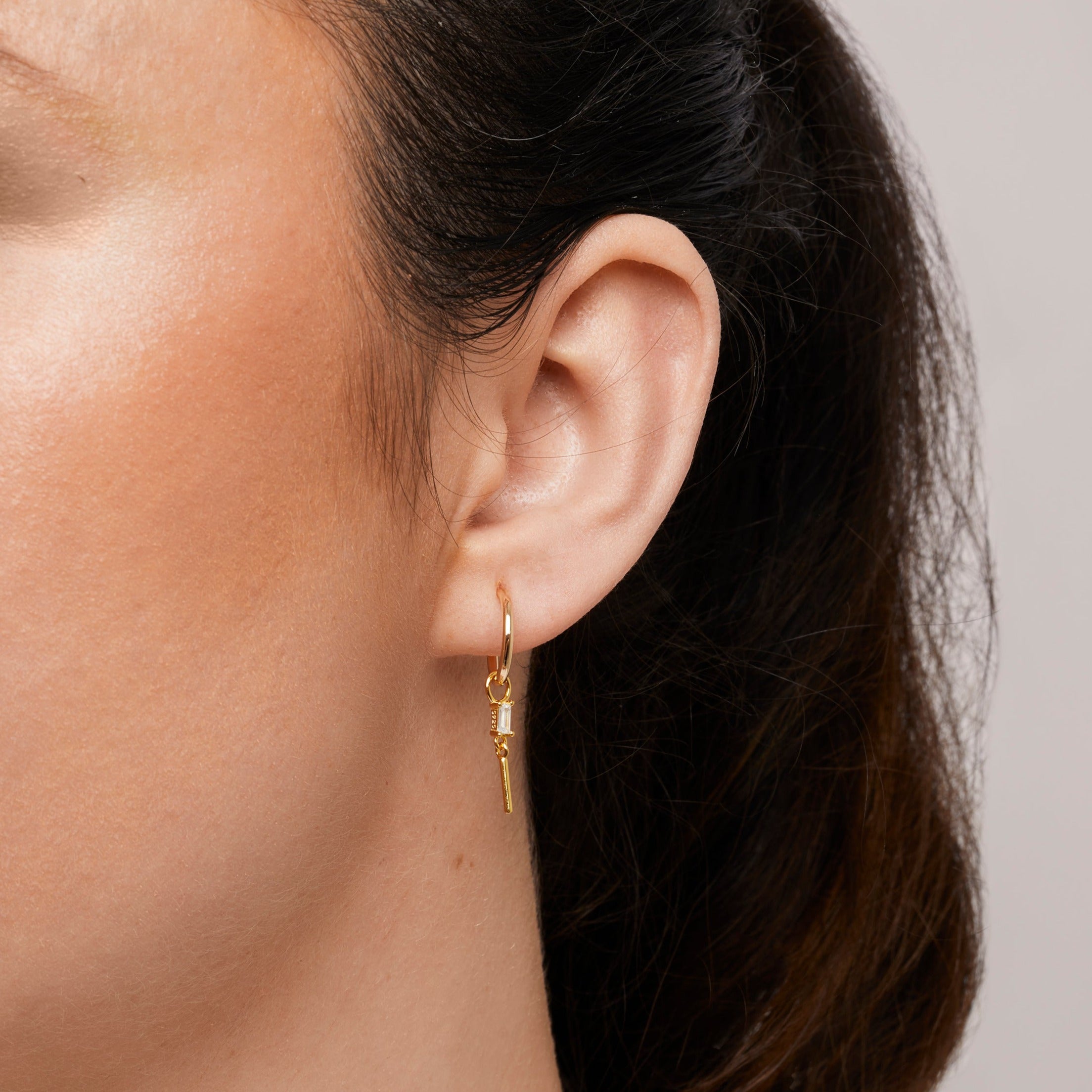 A model wearing the Rectangle Drop Hoop Charms are made with high-quality materials, including 18K gold plating over 925 Sterling Silver. These charms are both non-tarnish and water resistant. The perfect combination of style and durability.