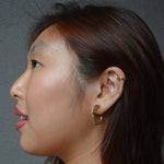 A model wearing the Twist Hoop Earrings feature a secure and comfortable screwback clip-on closure ideal for all ear types. Wear these earrings for up to 8-12 hours per day with a secure hold and the ability to be manually adjusted to the individual's size. Crafted from gold tone plated copper alloy, these earrings come is a single pair.