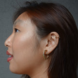 A model wearing the Twist Hoop Earrings feature a secure and comfortable screwback clip-on closure ideal for all ear types. Wear these earrings for up to 8-12 hours per day with a secure hold and the ability to be manually adjusted to the individual's size. Crafted from gold tone plated copper alloy, these earrings come is a single pair.