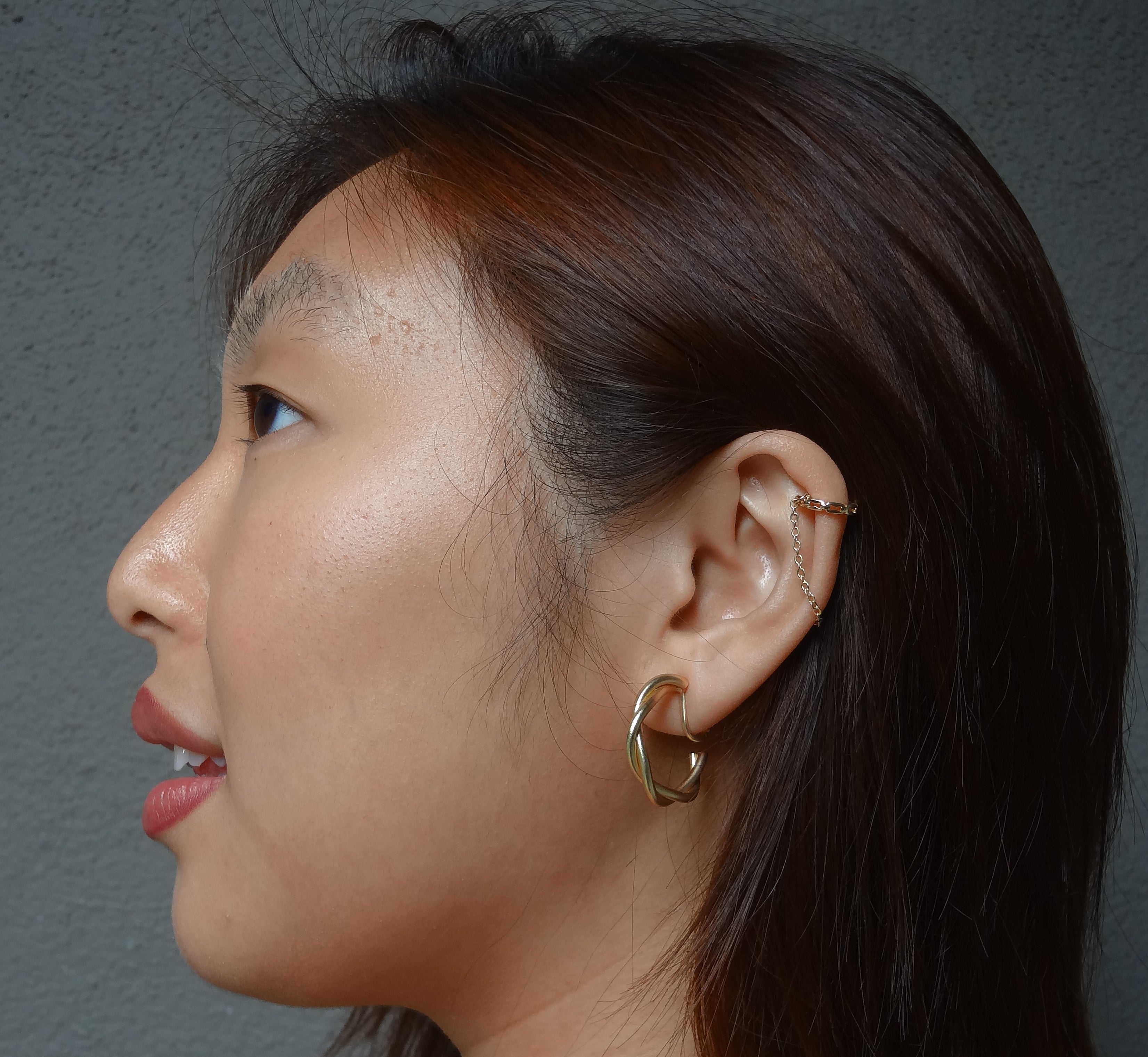 A model wearing the Twist Hoop Earrings feature a secure and comfortable screwback clip-on closure ideal for all ear types. Wear these earrings for up to 8-12 hours per day with a secure hold and the ability to be manually adjusted to the individual's size. Crafted from gold tone plated copper alloy, these earrings come is a single pair.