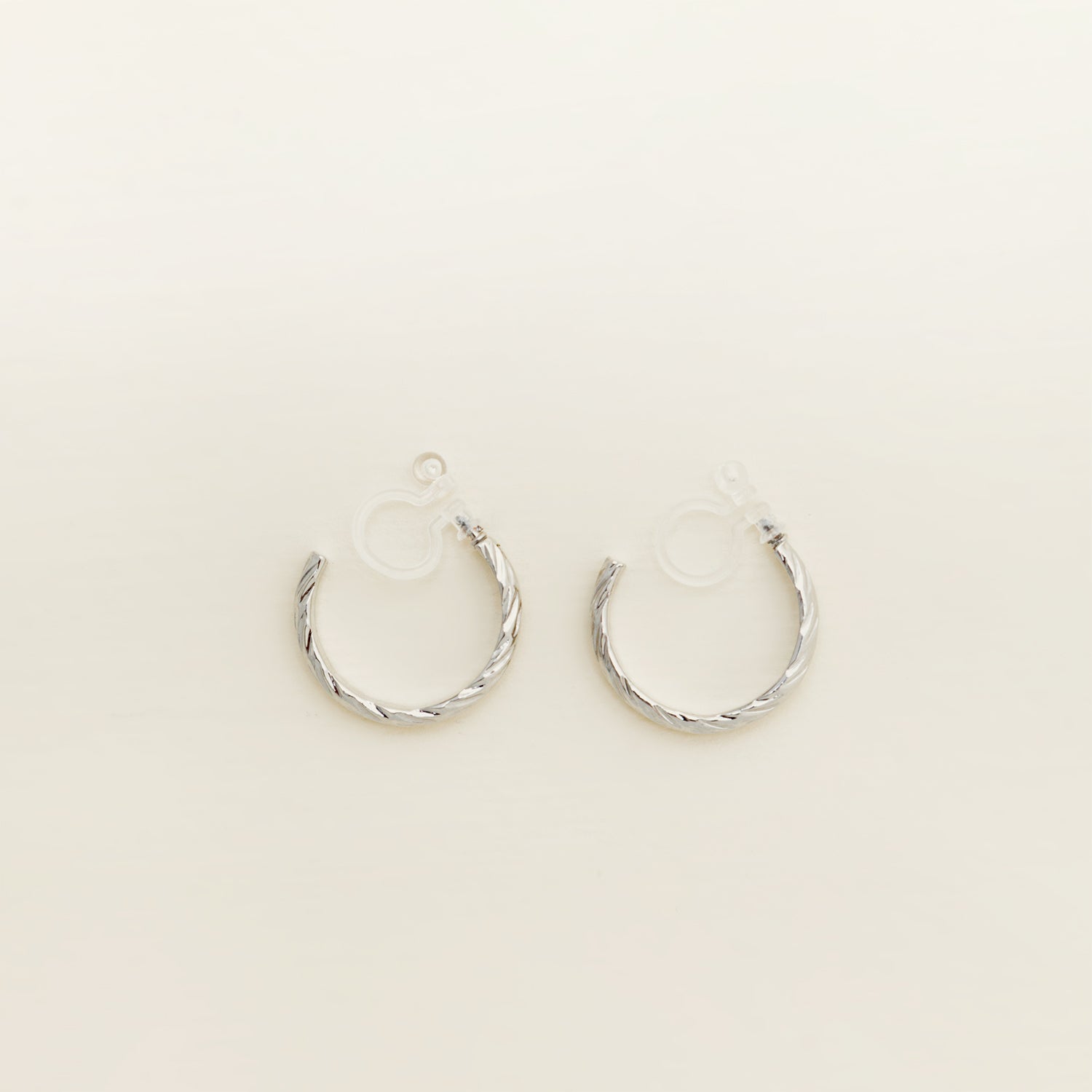 Image of the Silver Talia Hoop Clip-On Earrings boast a strong, medium-secure hold. They are crafted from a silver-tone alloy and feature a resin closure. They can be worn comfortably for 8-12 hours and are versatile enough for all ear shapes and sizes, including thick/large, sensitive, small/thin, and stretched/healing ears. An identical version is also available in Gold.