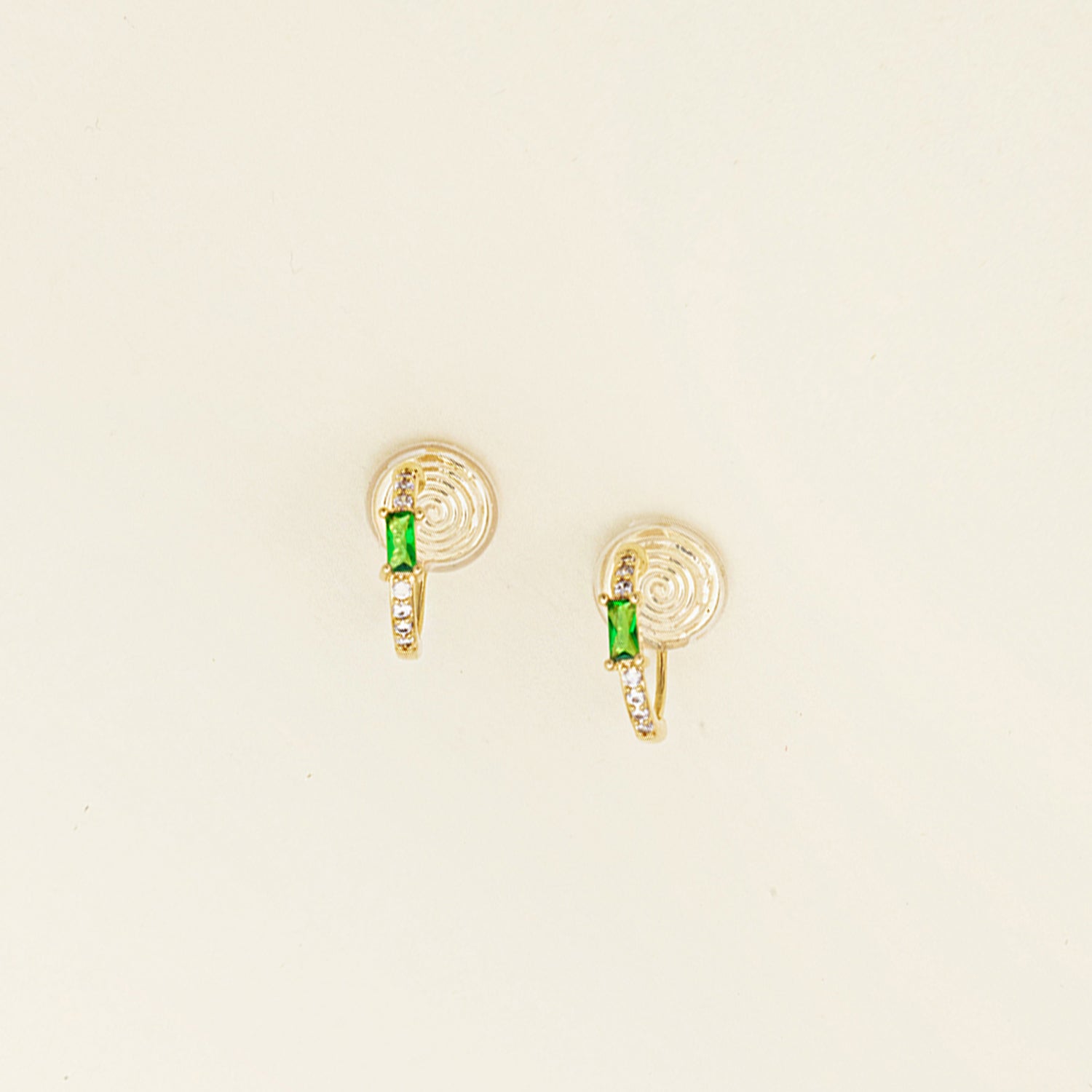 Image of the Emerald Pavé Huggie Clip-On Earrings features a closure type of mosquito coil clip-on earrings. They are suitable for all types of ear shapes and sizes, and are comfortable to wear for up to 24 hours. The hold strength is medium, allowing you to gently adjust the padding forward once on the ear. Crafted with 18k gold plated metal alloy and cubic zirconia, these earrings are non-tarnish and water-resistant.