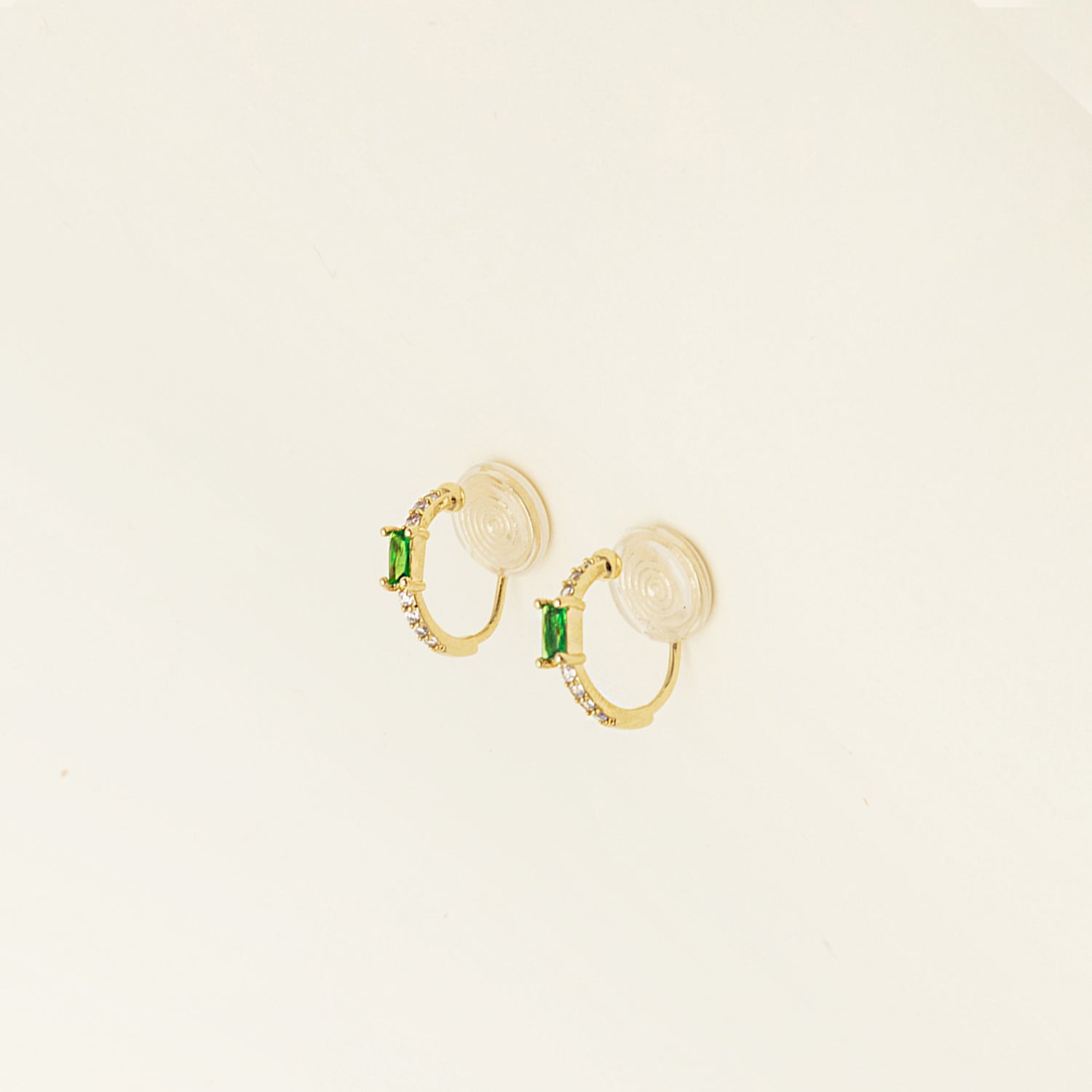 Image of the Emerald Pavé Huggie Clip-On Earrings features a closure type of mosquito coil clip-on earrings. They are suitable for all types of ear shapes and sizes, and are comfortable to wear for up to 24 hours. The hold strength is medium, allowing you to gently adjust the padding forward once on the ear. Crafted with 18k gold plated metal alloy and cubic zirconia, these earrings are non-tarnish and water-resistant.