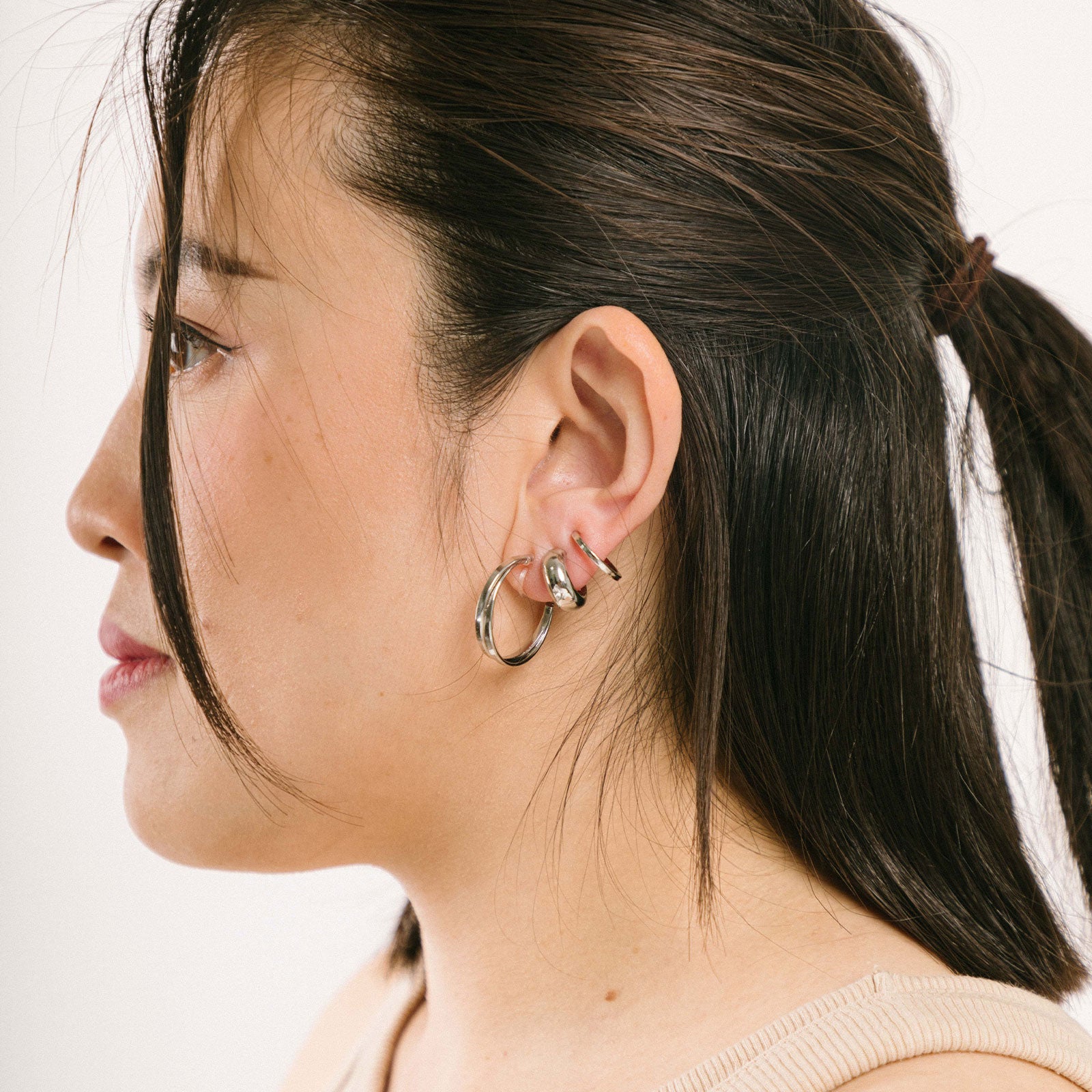 A model wearing the Everyday Essentials Set features three closure types: invisible resin, sliding spring and mosquito coil. It includes a Simple Silver Huggie Clip-On, Mini Hoop Earrings and Silver Cassie Hoop Earrings. Crafted from copper alloy, stainless steel and silver tone metal alloy, this item comes with three pairs and is also available in Gold.