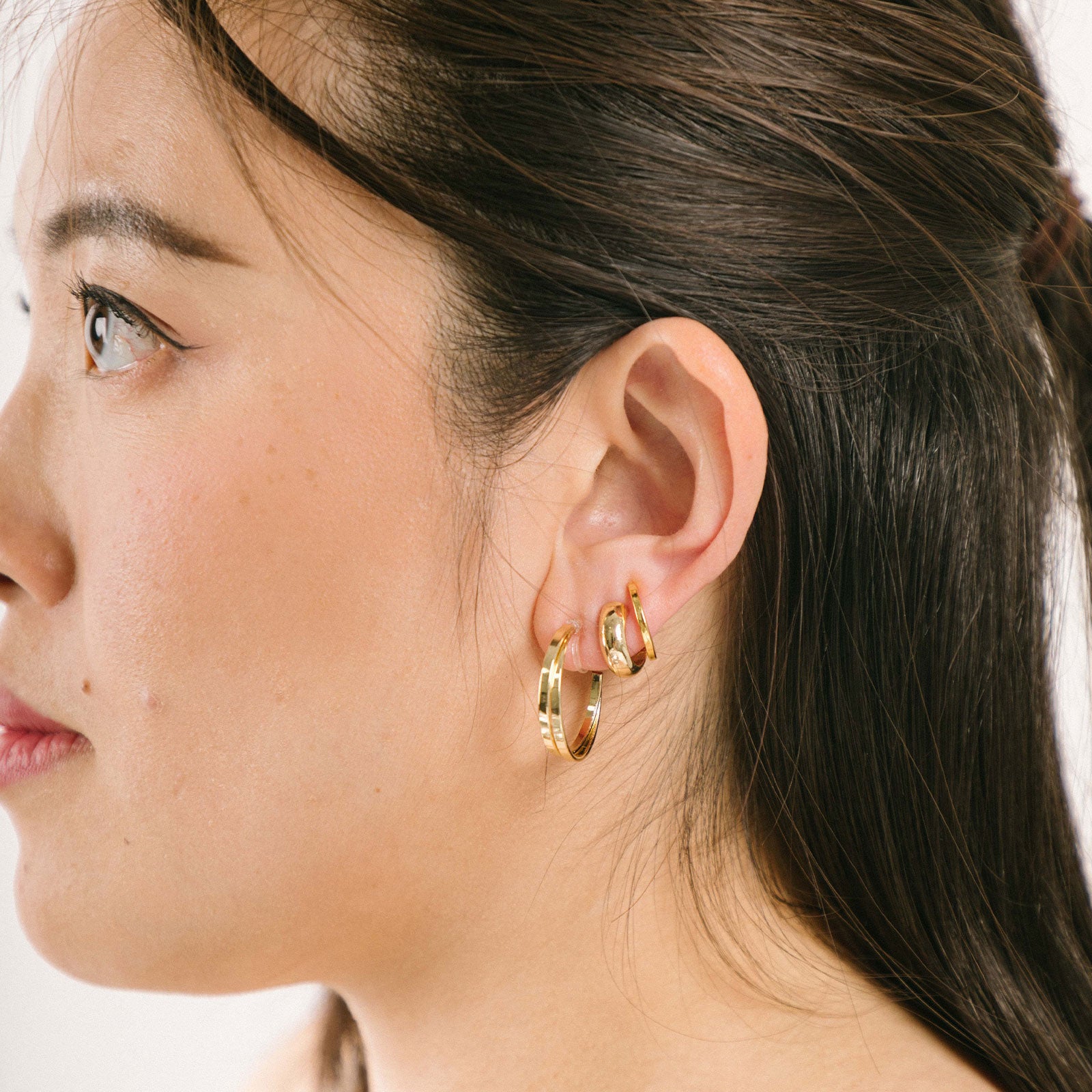 A model wearing the Everyday Essentials Set comes with three pairs of earrings featuring an Invisible Resin, Sliding Spring and Mosquito Coil closure. The set includes a Simple Gold Huggie Clip-On, Mini Hoop Earrings, and Gold Cassie Hoop Earrings, all crafted of Gold tone plated alloy, Stainless steel, or Gold Tone Metal Alloy. It is also available in Silver.