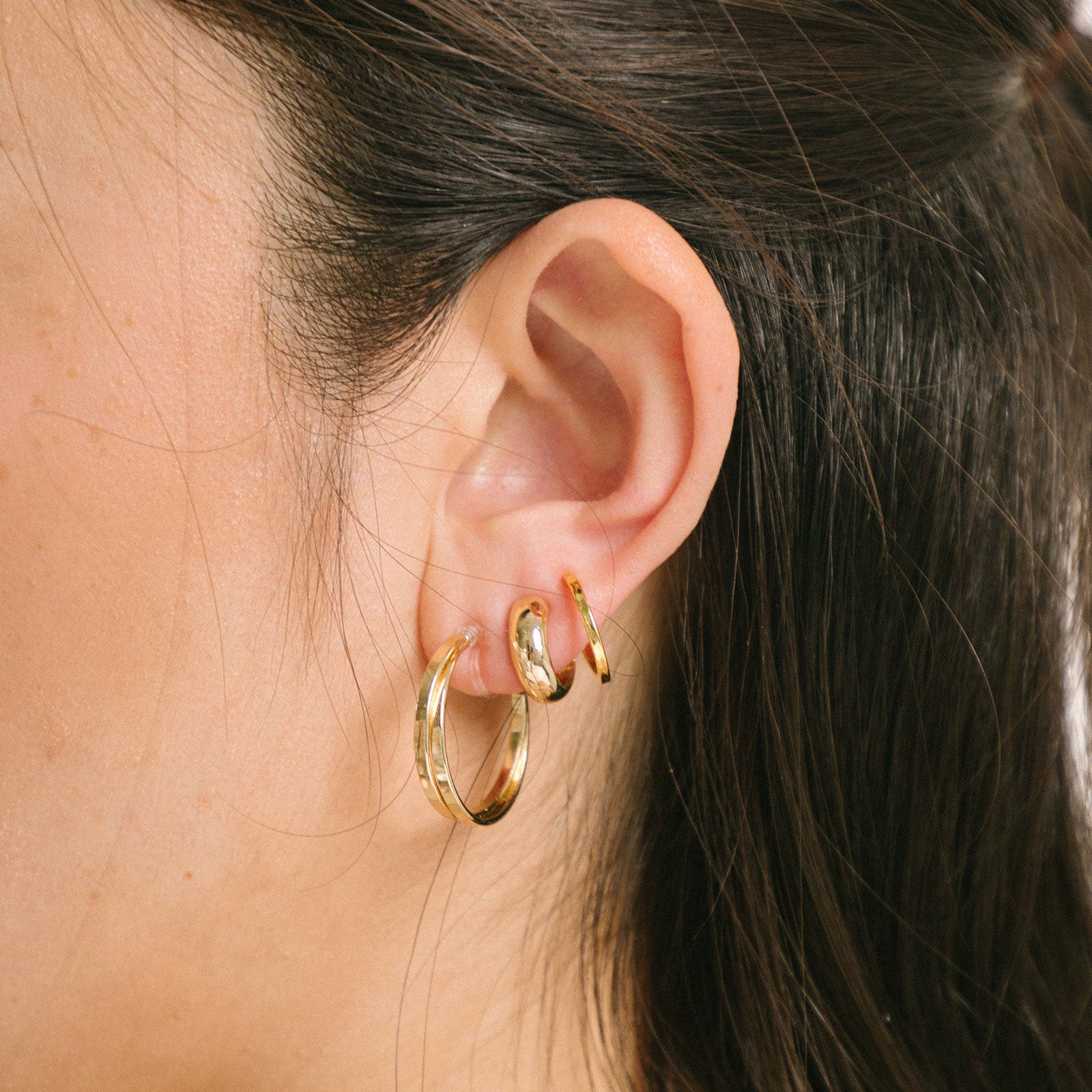 A model wearing the Everyday Essentials Set comes with three pairs of earrings featuring an Invisible Resin, Sliding Spring and Mosquito Coil closure. The set includes a Simple Gold Huggie Clip-On, Mini Hoop Earrings, and Gold Cassie Hoop Earrings, all crafted of Gold tone plated alloy, Stainless steel, or Gold Tone Metal Alloy. It is also available in Silver.