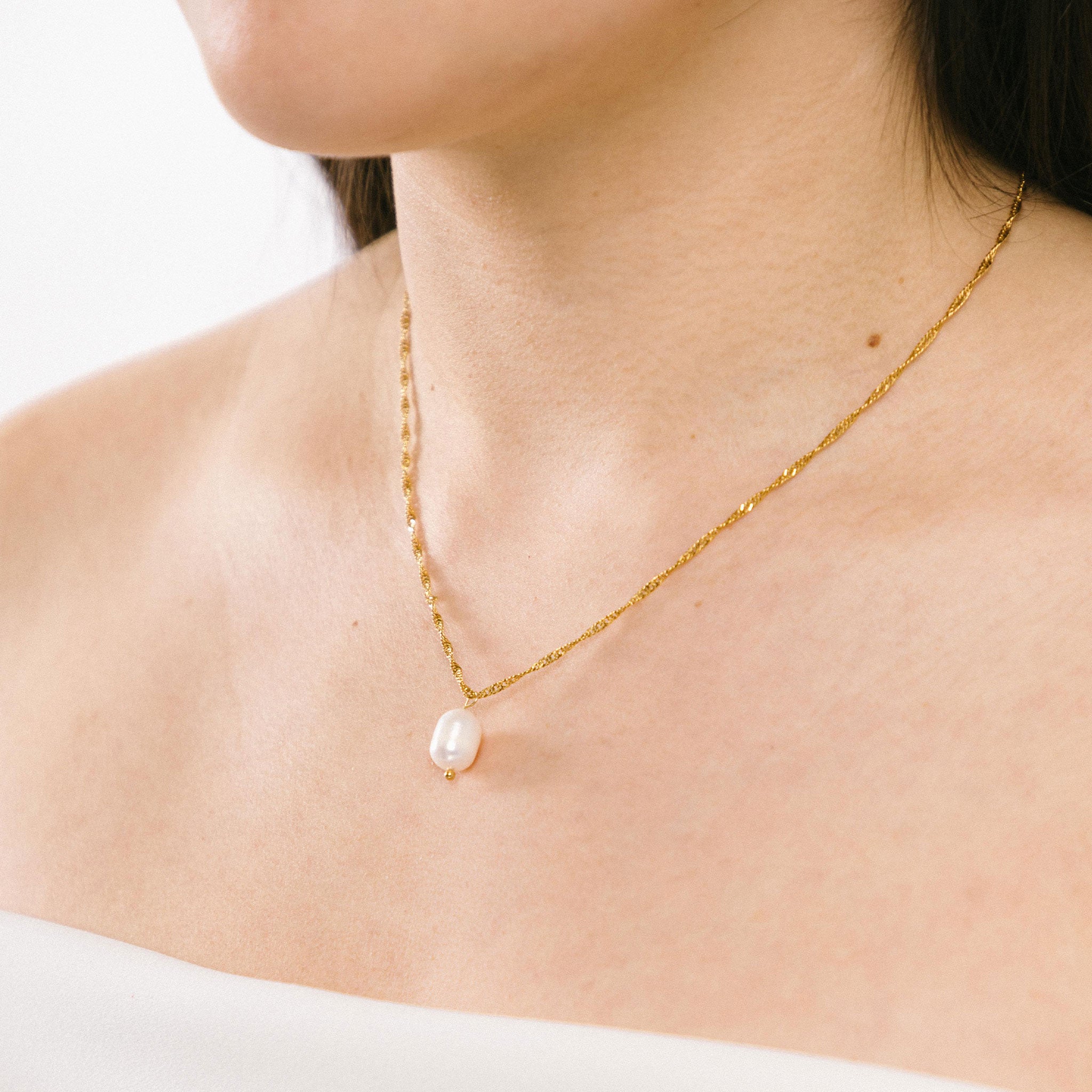 A model wearing the Ava Pearl Necklace, an elegant piece, decorated with a Freshwater Pearl and framed in 18K Gold Plated Stainless Steel. Its water-resistance and hypoallergenic qualities make it a luxurious and comfortable complement to any jewelry repertoire.