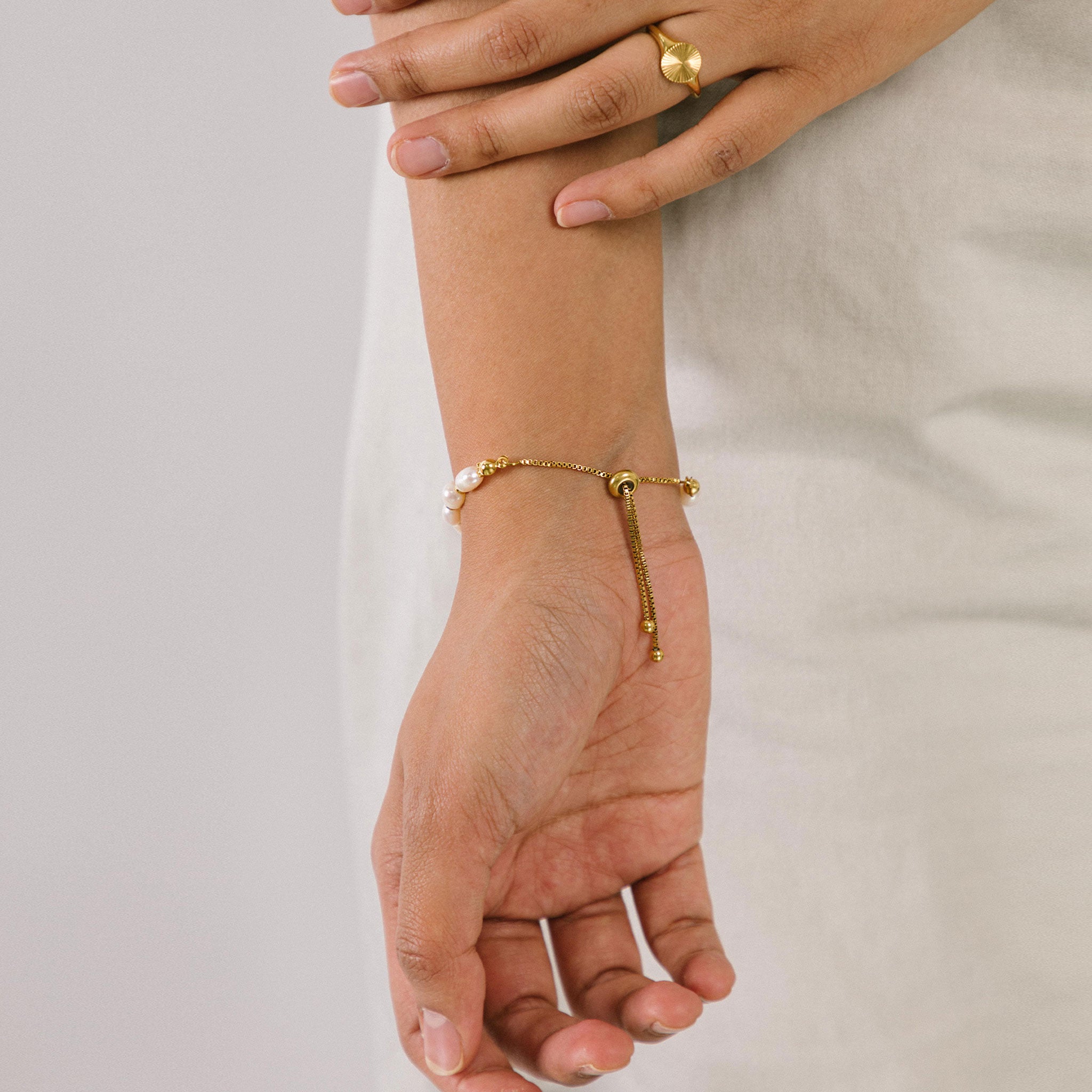 A model wearing the Emi Pearl Bracelet is crafted from 18K Gold Plated Stainless Steel and Freshwater Pearls, allowing for a small degree of variation in size and hue. The bracelet is water-resistant and hypoallergenic.