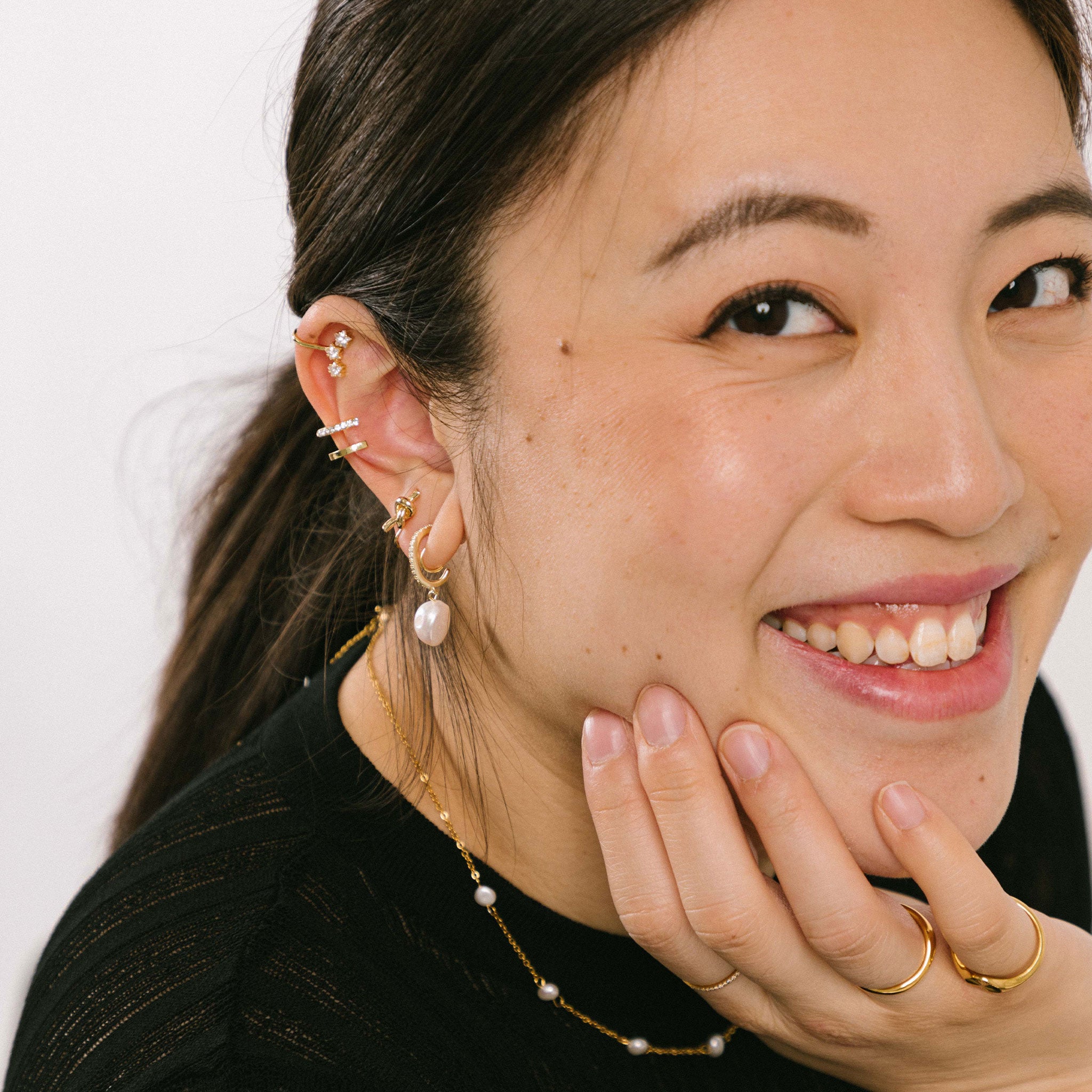 A model wearing the Pearl Pavé Huggie Clip-On Earrings in Gold offer a secure yet adjustable hold with an average comfortable wear duration of 24 hours. Featuring high-quality Freshwater Pearls and 18K Gold Plated Stainless Steel, these earrings are ideal for all ear types and sizes. Each piece may vary slightly in size and color.