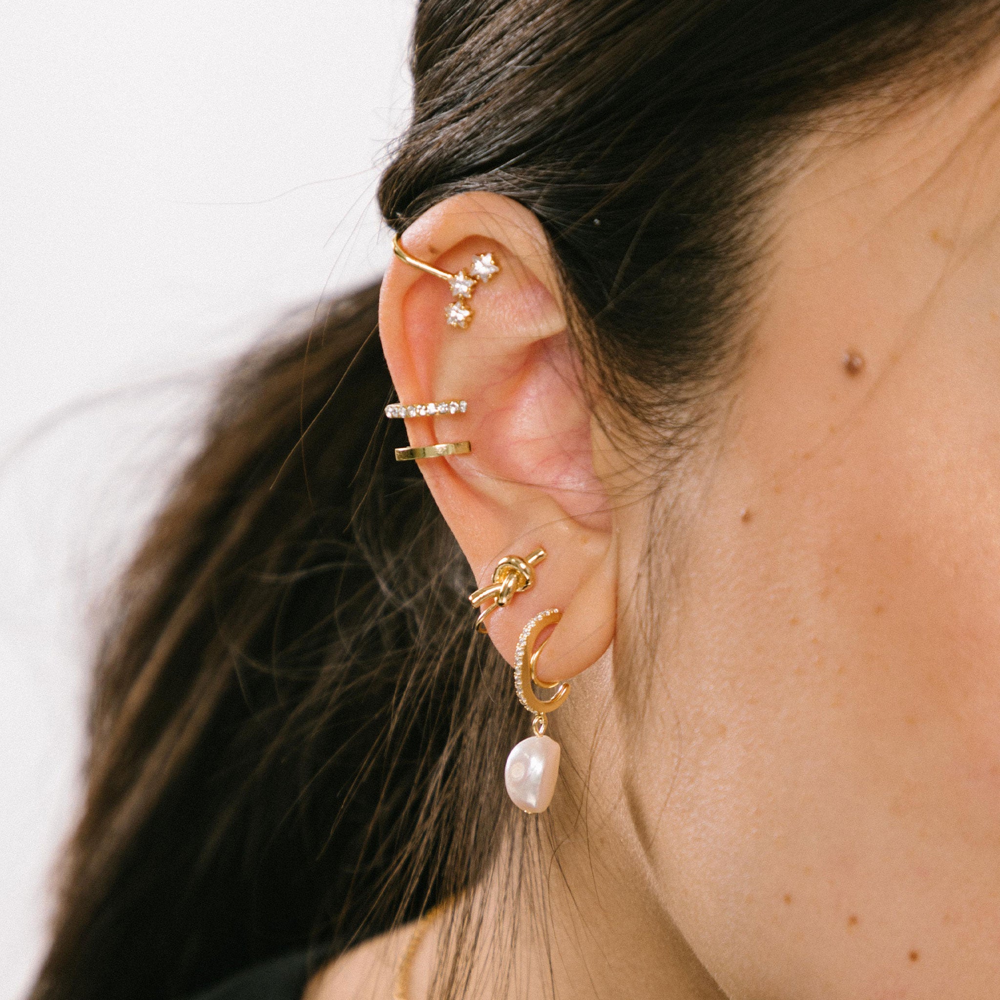 A model wearing the Pearl Pavé Huggie Clip-On Earrings in Gold offer a secure yet adjustable hold with an average comfortable wear duration of 24 hours. Featuring high-quality Freshwater Pearls and 18K Gold Plated Stainless Steel, these earrings are ideal for all ear types and sizes. Each piece may vary slightly in size and color.